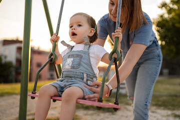 Fototapeta na wymiar mother and daughter little toddler girl child on swing in park