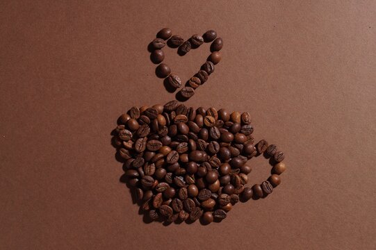 Cup of hot drink, composition made with coffee beans on brown background, flat lay