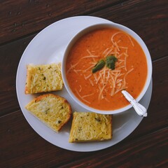 Roasted tomato basil soup served with garlic bread on wooden coffee table