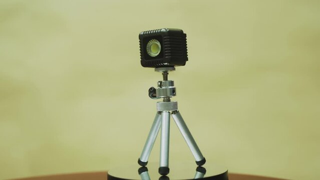 LED cube on a mini tripod, on a 360 rotating stand, slow motion, with beige background, 4K