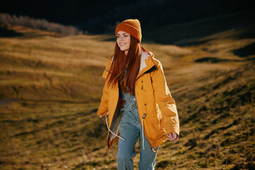 Woman running up the hill to the camera smile with teeth in the mountains in the autumn in a yellow raincoat and jeans happy sunset trip on a hike mountains in the snow, freedom lifestyle 