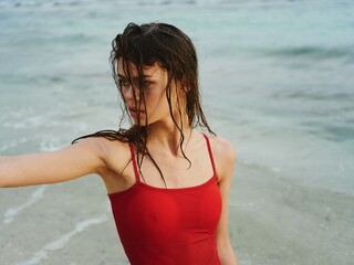 Woman model in red swimsuit posing in the water in the ocean and looking out at the horizon,...