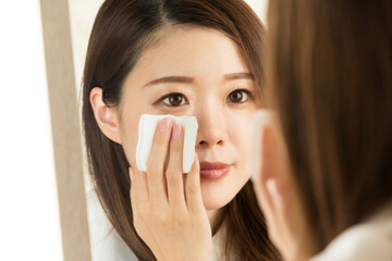 女性は鏡を見て、コットンで顔を拭いている。