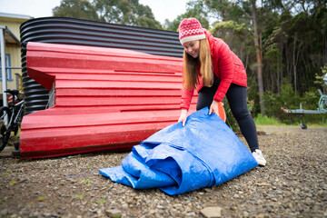 woman folding up a tarp at a campground in australia. camping tant and tarp while caravaning and...