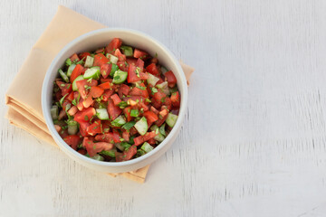 Healthy food tomato cucumber salad in bowl on white wood background.