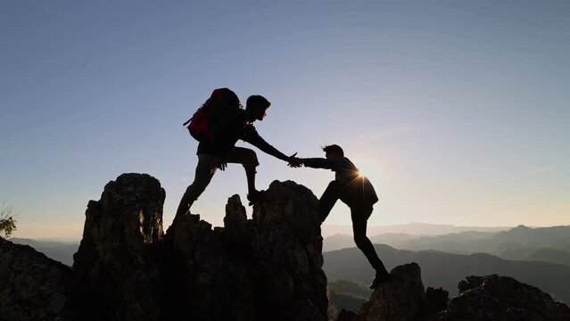 Silhouette of couple hiking help each other silhouette in mountains with sunlight. helping hand between two climber. two hikers on top of the mountain, a man helps a man to climb a sheer stone.