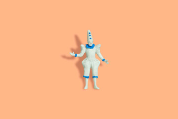Miniature people toy figure photography. Full body of a white clown wearing cone hat. Isolate on orange pastel background