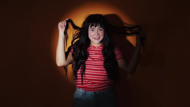 Young Crazy Woman Holding Long Black Hair While Standing And Laughing Against Spotlight In Studio. medium shot