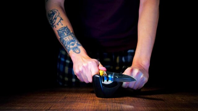 A man sharpens knives on a black background