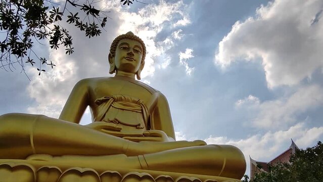 front view Golden big Buddha statue (Phra Buddha Dhammakaya Thep Mongkol) in Wat Pak Nam Phasi Charoen temple. Sunlight sky and cloud background