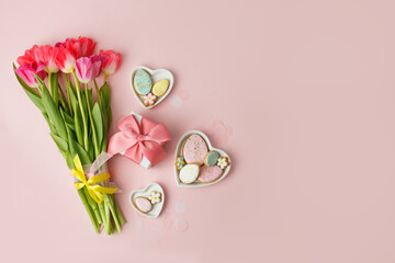 Happy Easter. Multi-colored pastel easter cookies gingerbread, gift box seasonal flowers tulips on pink background. Easter concept, copy space, flyer, banner, coupon, greeting card, invitation - 553899145