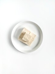 White and smooth tofu that is cut into smaller pieces placed on a white ceramic plate isolated on white background. Top view