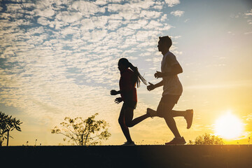 Fototapeta na wymiar Silhouette of young couple running together on road. Couple, fit runners fitness runners during outdoor workout with sunset background.