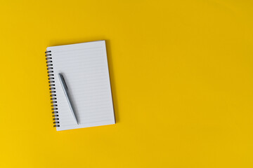 Blank notebook and a pen on yellow background