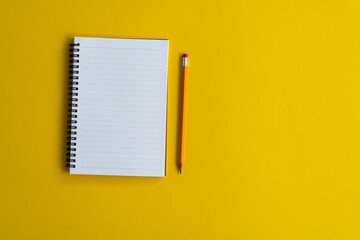 Blank notebook and a pen on yellow background