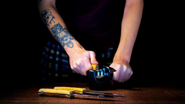 A man sharpens knives on a black background