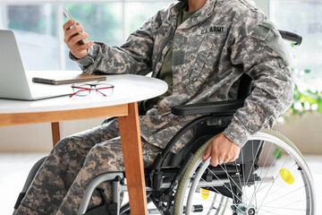 Young soldier in wheelchair using mobile phone at home