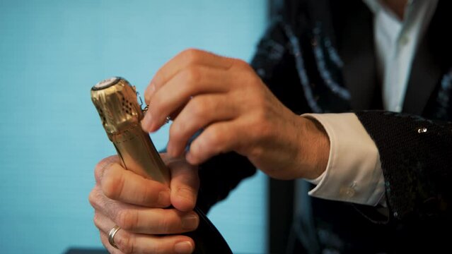 Opening champagne bottle tinfoil wrap, muselet and cork in tuxedo.
