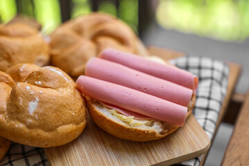 Delicious kaiser rolls with butter and ham on wooden board