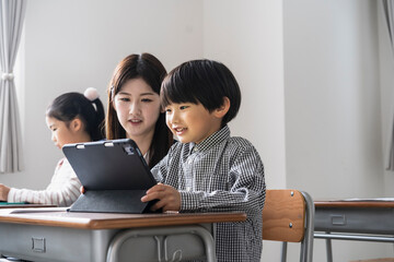 タブレットPCを使った授業をする日本人小学生の男の子と女性教師