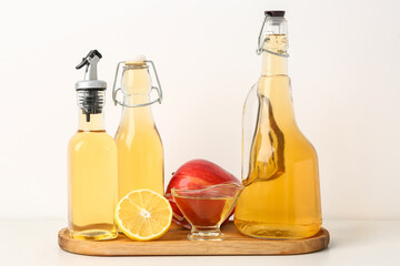 Obraz na płótnie Canvas Wooden board with bottles of apple cider vinegar and fruits on light background
