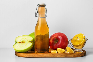 Wooden board with bottle of apple cider vinegar and fresh fruits on light background