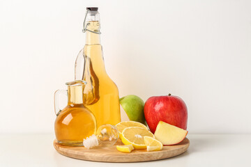 Wooden board with bottles of apple cider vinegar and fresh fruits on light background