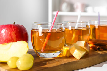 Wooden board with glasses of fresh apple juice and fruits on table in kitchen, closeup