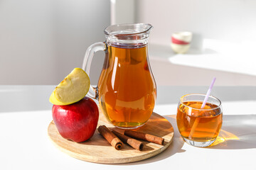 Jug and glass of fresh apple juice and cinnamon on table