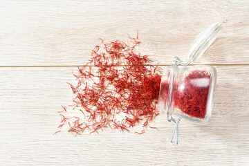 Dried saffron spices spill out of a glass storage jar on a wooden table , top view.