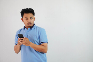 expression of dislike trying to dodge with holding phone young asian man wearing blue polo t shirt isolated on white background - obrazy, fototapety, plakaty