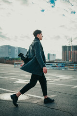 A guy in an autumn coat walks through the parking lot against the background of railings