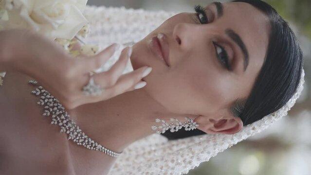 young woman in a wedding dress and jewelry posing at the camera. vertical video