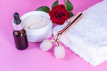 Obraz na płótnie Canvas Packaging with blindfolds under the eyes. Cosmetic product. Pink Y-shaped ball roller for facial massage and eye bandages on the table with a towel. The roller is made of rose quartz. Selective focus.