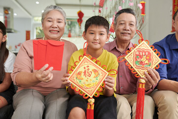Grandparents and grandson showing pedants and red envelopes for Tet celebration - obrazy, fototapety, plakaty