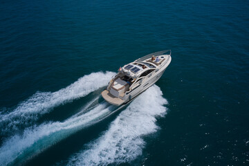 Big white yacht with people moving on blue water top view. Summer travel on a yacht aerial view. Yacht in the sea aerial view.