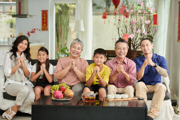 Smilng family making greeting gesture and looking at camera when celebrating Tet at home