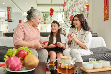 Happy senior woman gifting lucky money envelopes to daughter and granddaughter