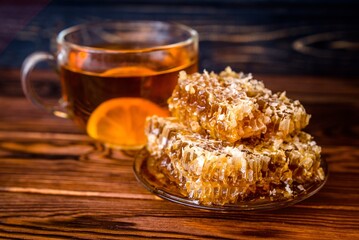 honey in honeycombs and a mug of tea on a brown wooden background
