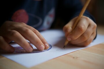 Children's hands make a drawing using a protractor on white paper with a simple pencil.