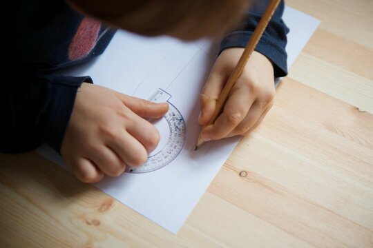 Children's hands make a drawing using a protractor on white paper with a simple pencil.