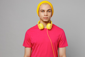 Young attractive handsome calm serious man of African American ethnicity 20s he wears pink t-shirt yellow hat headphones look camera isolated on plain pastel light purple background studio portrait.