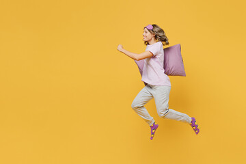 Fototapeta na wymiar Full body young happy woman she wear purple pyjamas jam sleep eye mask rest relax at home jump high run fast hurry up hold pillow isolated on plain yellow background studio portrait Night nap concept