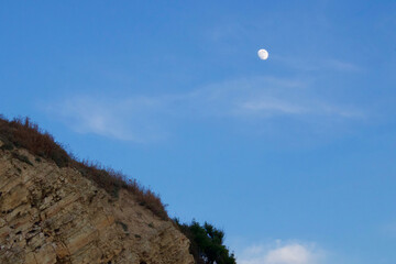 Little moon in the sky. Crescent above a cliff with a steep slope.