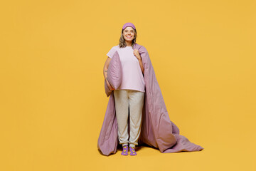 Full body young fun woman wears purple pyjamas jam sleep eye mask rest relax at home hold in hand blanket duvet pillow go to bed isolated on plain yellow background studio portrait. Night nap concept.