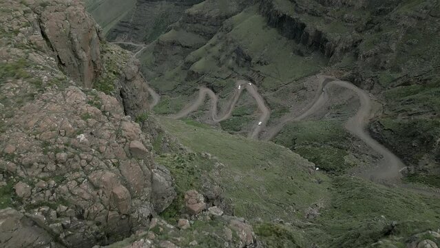 Aerial reveal: Vehicles on gravel switchback Sani Pass road, Lesotho