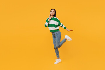Full body side view smiling fun young latin woman in casual cozy green knitted sweater look camera raise up leg hold face isolated on plain yellow background studio portrait People lifestyle concept