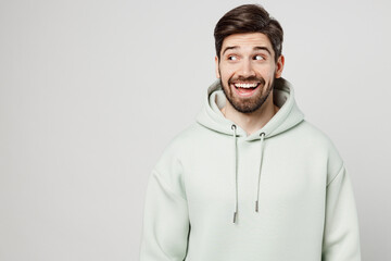 Young impressed happy fun cool unshaven caucasian man wear mint hoody look aside on workspace area...
