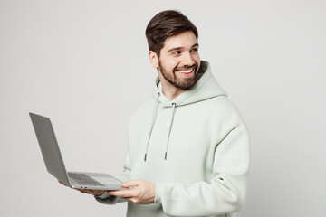 Young programmer happy caucasian man wear mint hoody hold use work on laptop pc computer look aside...