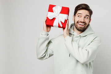 Young caucasian man wear mint hoody hold in hand red present box with gift ribbon bow look aside on workspace area isolated on plain solid white background studio portrait. People lifestyle concept. - Powered by Adobe